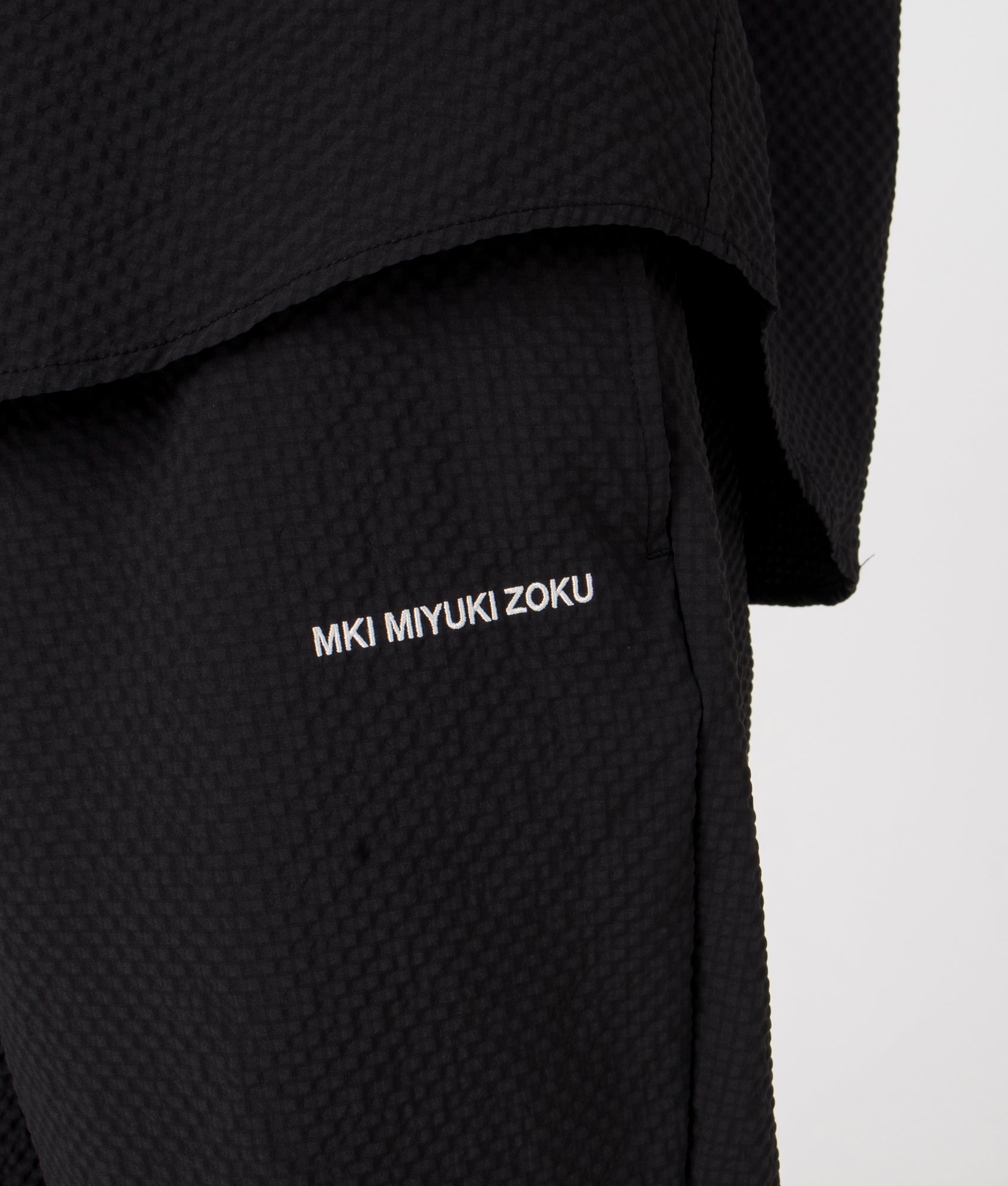 MKI Relaxed Fit Seersucker Trousers in Black. Detail angle model shot at EQVVS.