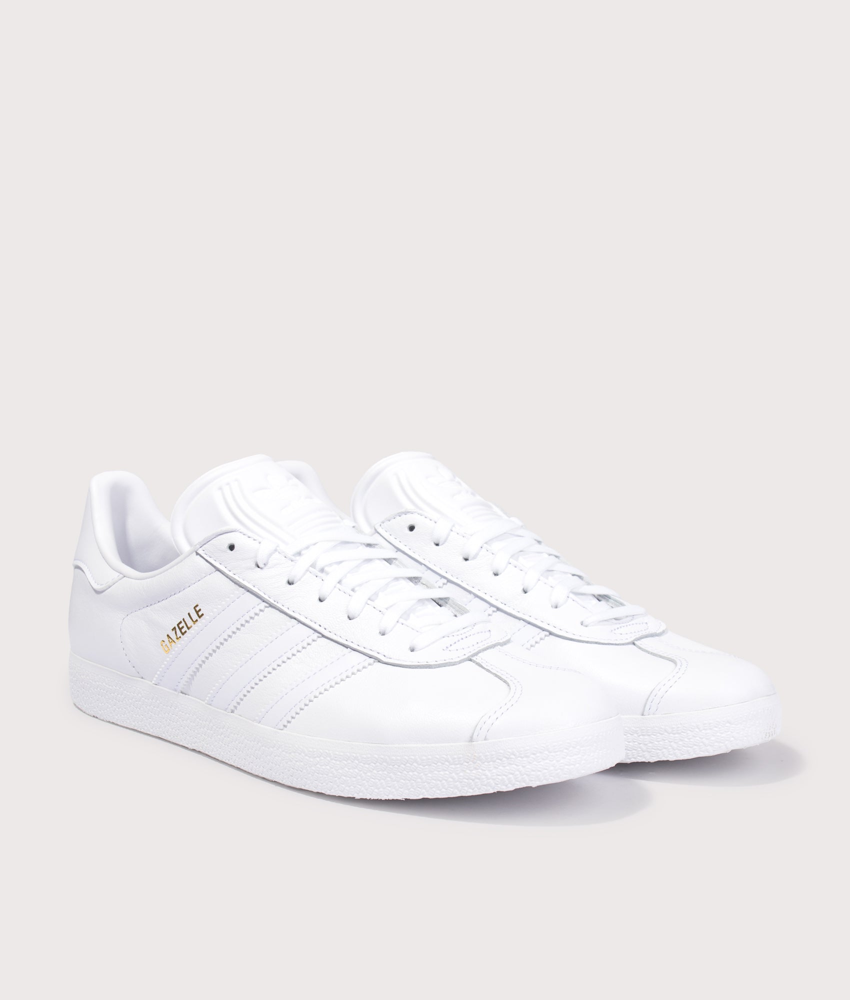 adidas Originals Gazelle Trainers in White/White/Gold Metallic at EQVVS Menswear. Angled front shot.