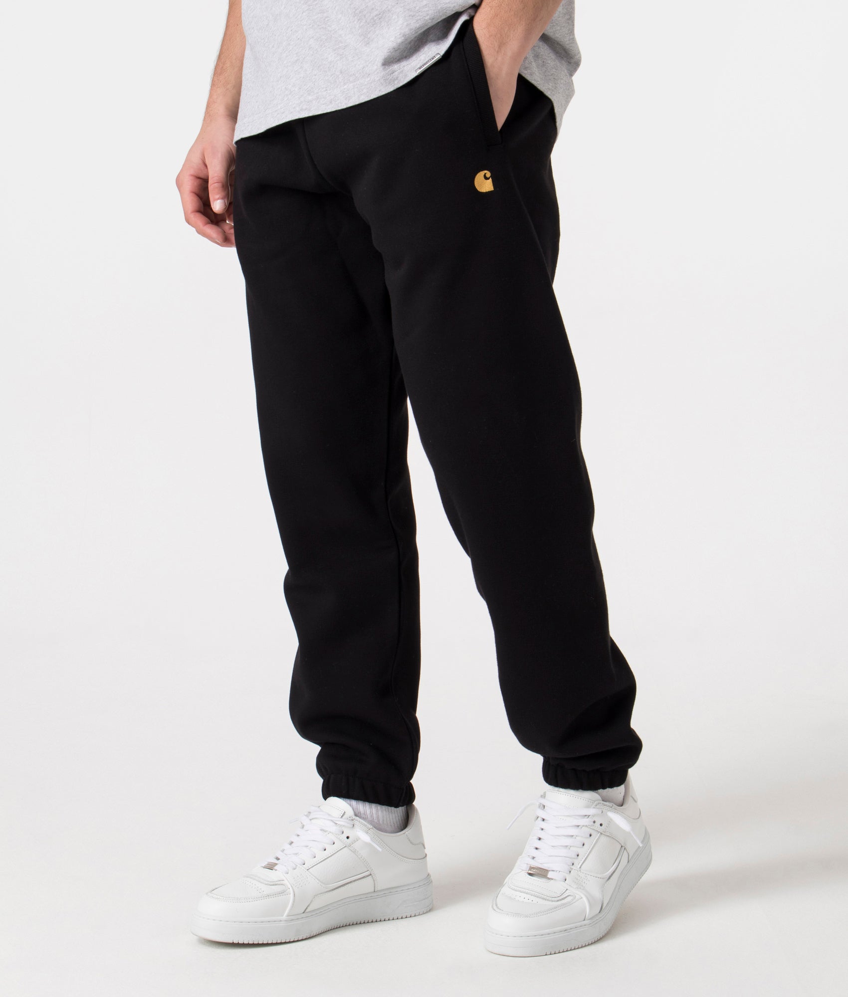 Carhartt WIP Relaxed Fit Chase Joggers in Black with Gold Carhartt 'C' Angle Shot at EQVVS