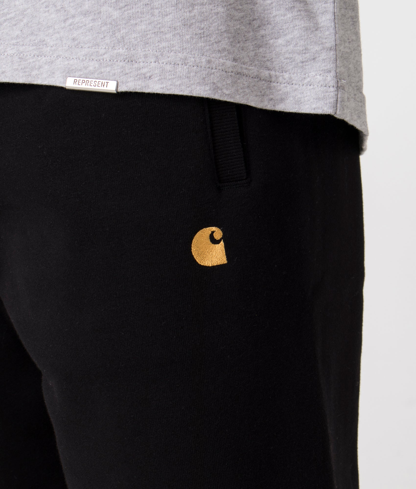 Carhartt WIP Relaxed Fit Chase Joggers in Black with Gold Carhartt 'C' Detail Shot at EQVVS