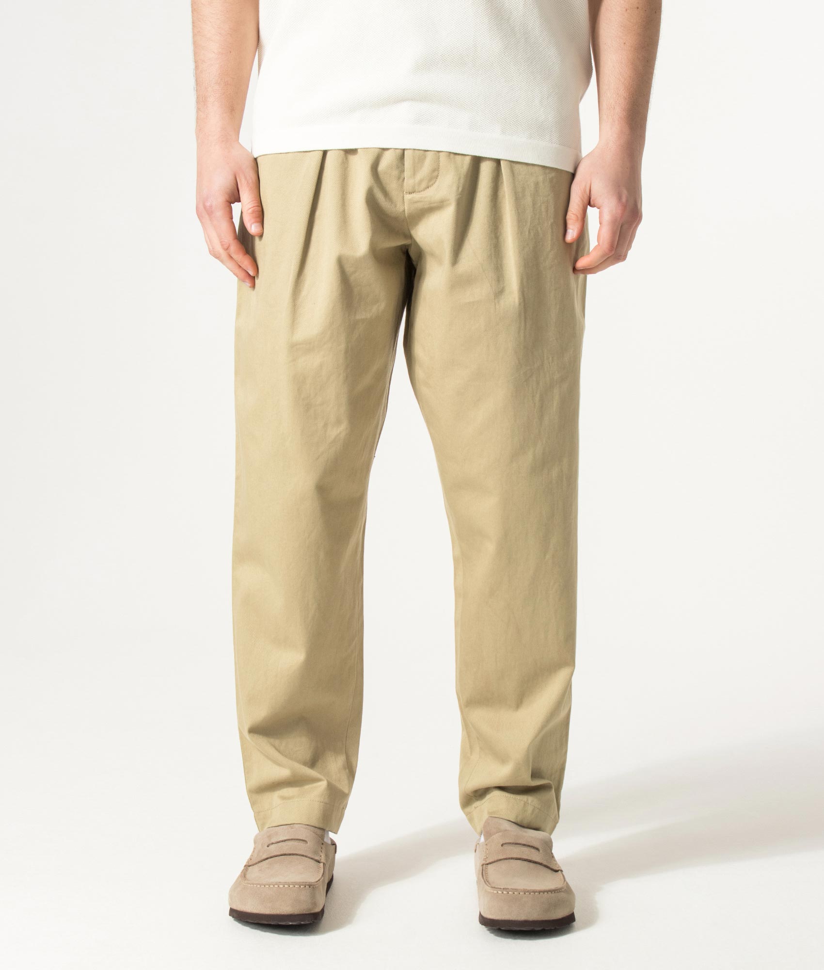 Universal Works Loose Tapered Pleated Track Pants in Sand at EQVVS Menswear. Model front shot.