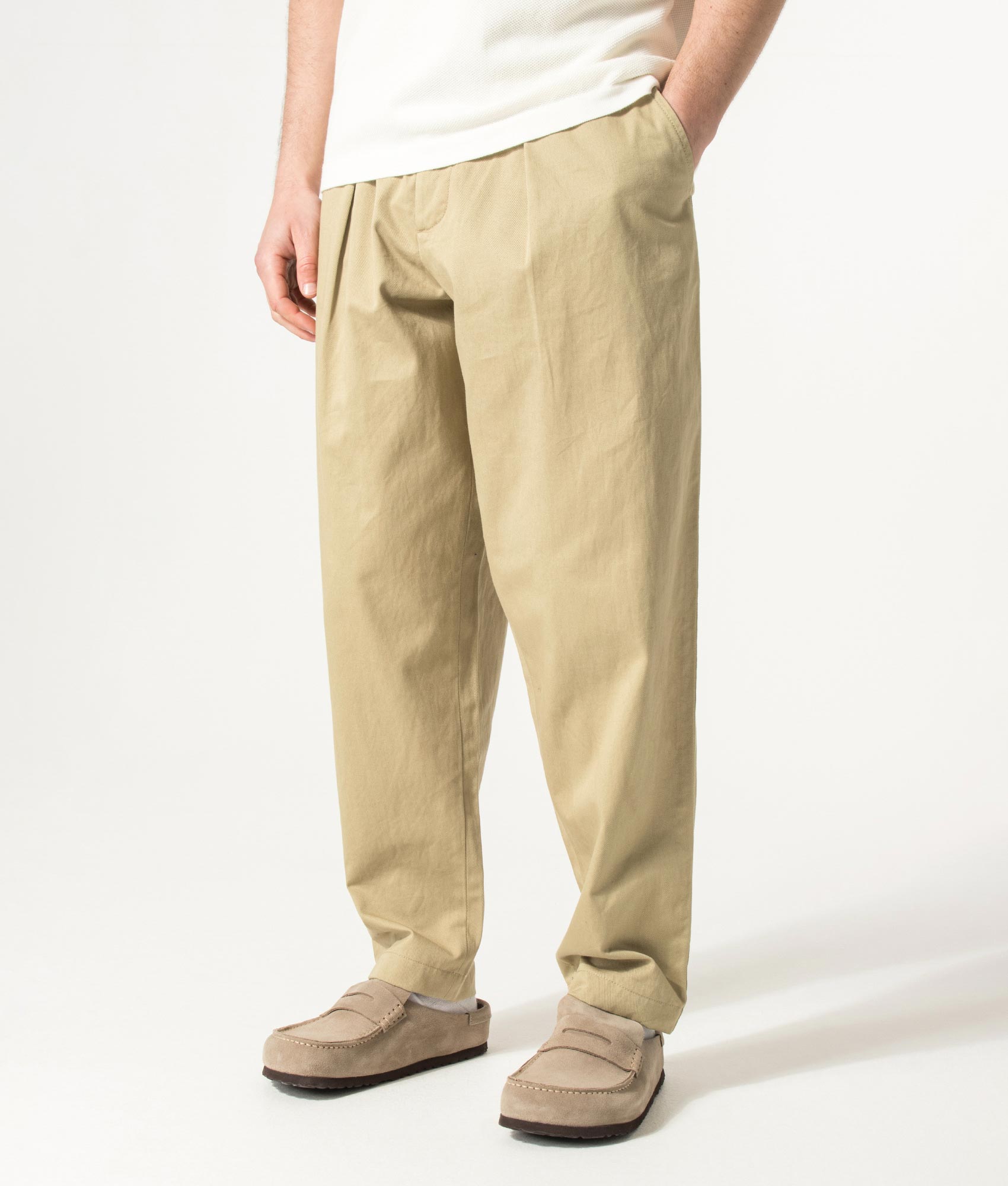 Universal Works Loose Tapered Pleated Track Pants in Sand at EQVVS Menswear. Angled model front shot.