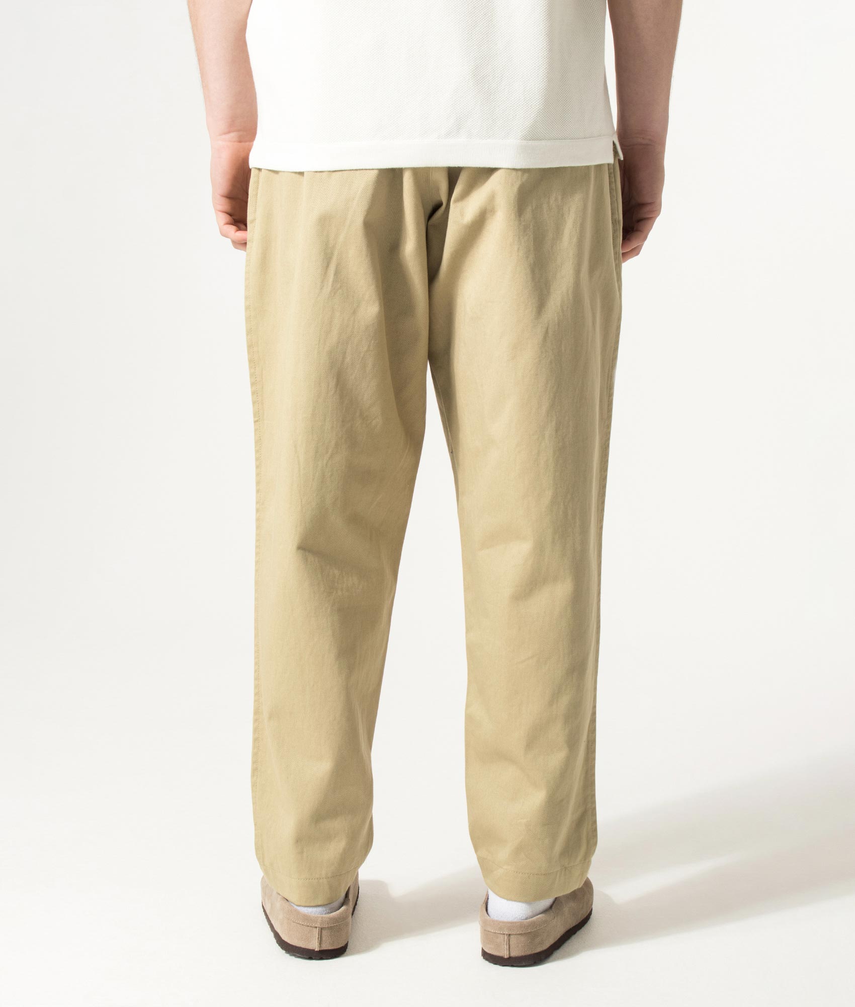 Universal Works Loose Tapered Pleated Track Pants in Sand at EQVVS Menswear. Model back shot.