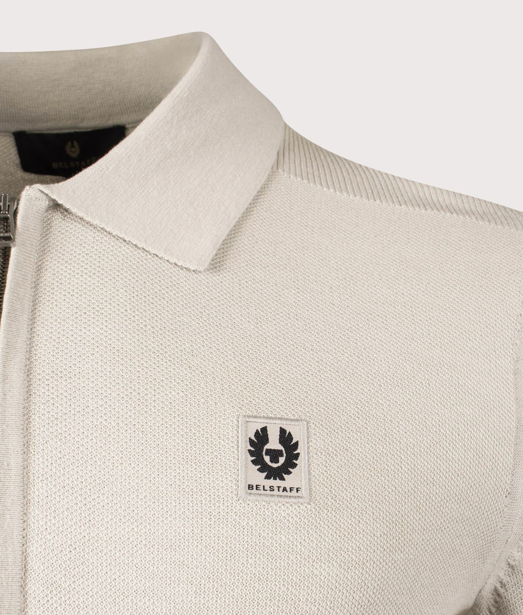 Belstaff Drift Knitted Long Sleeve Polo Shirt in Stone Beige. Shot at EQVVS. Detailed logo shot. 