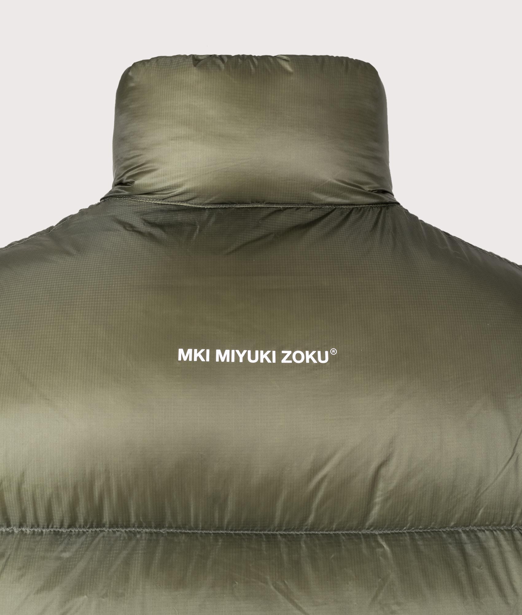 MKI MIYUKI ZOKU Translucent Funnel Neck Bubble Jacket in Olive at EQVVS Menswear. Back detail shot.