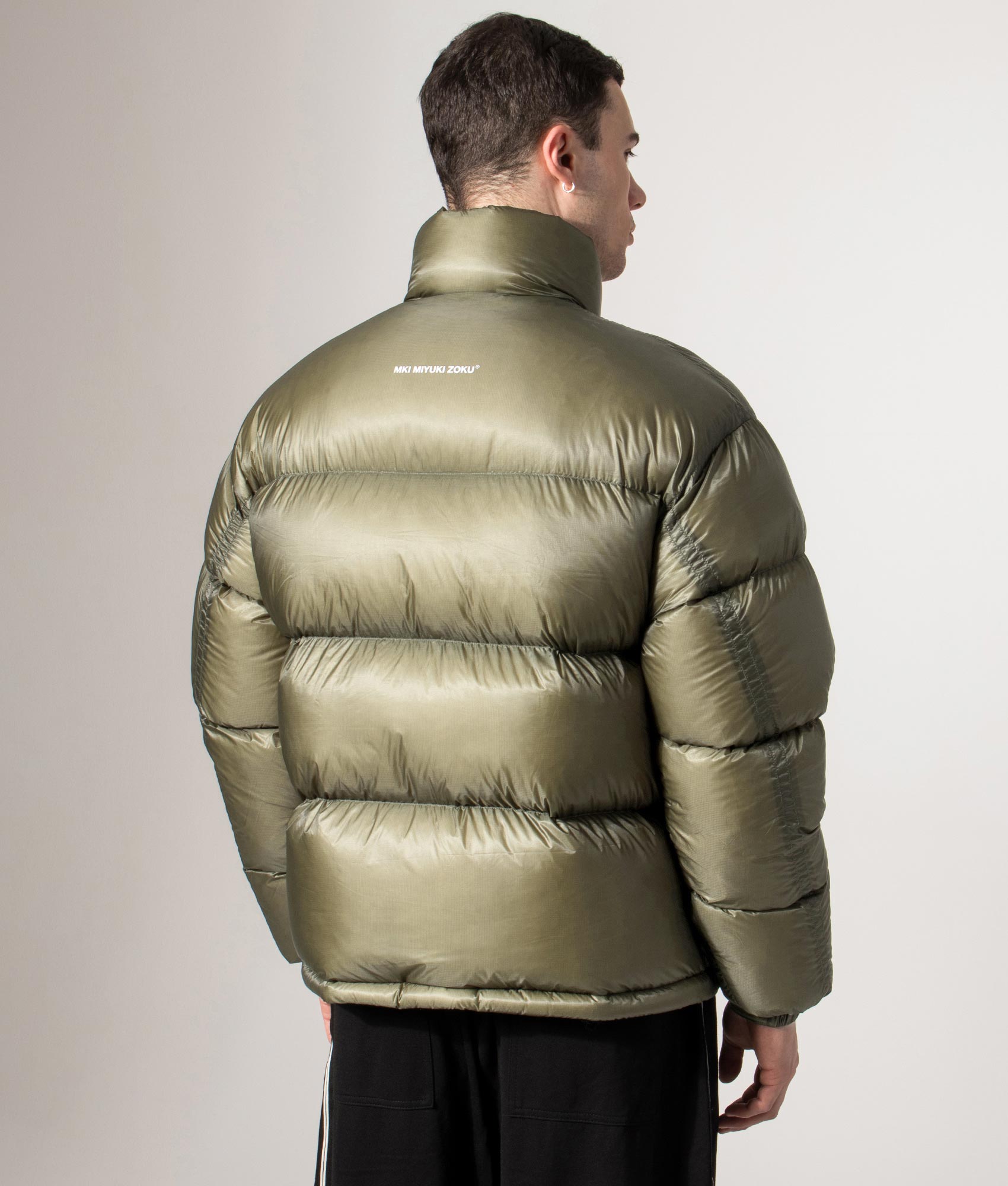 MKI MIYUKI ZOKU Translucent Funnel Neck Bubble Jacket in Olive at EQVVS Menswear. Back model shot.
