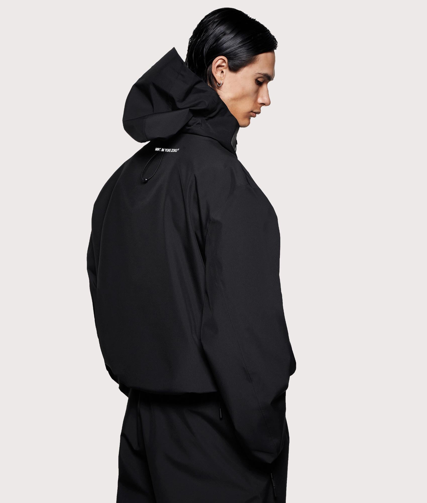 MKI MIYUKI ZOKU V3 Shell Hooded Jacket in Black at EQVVS Menswear. Angled model back shot.