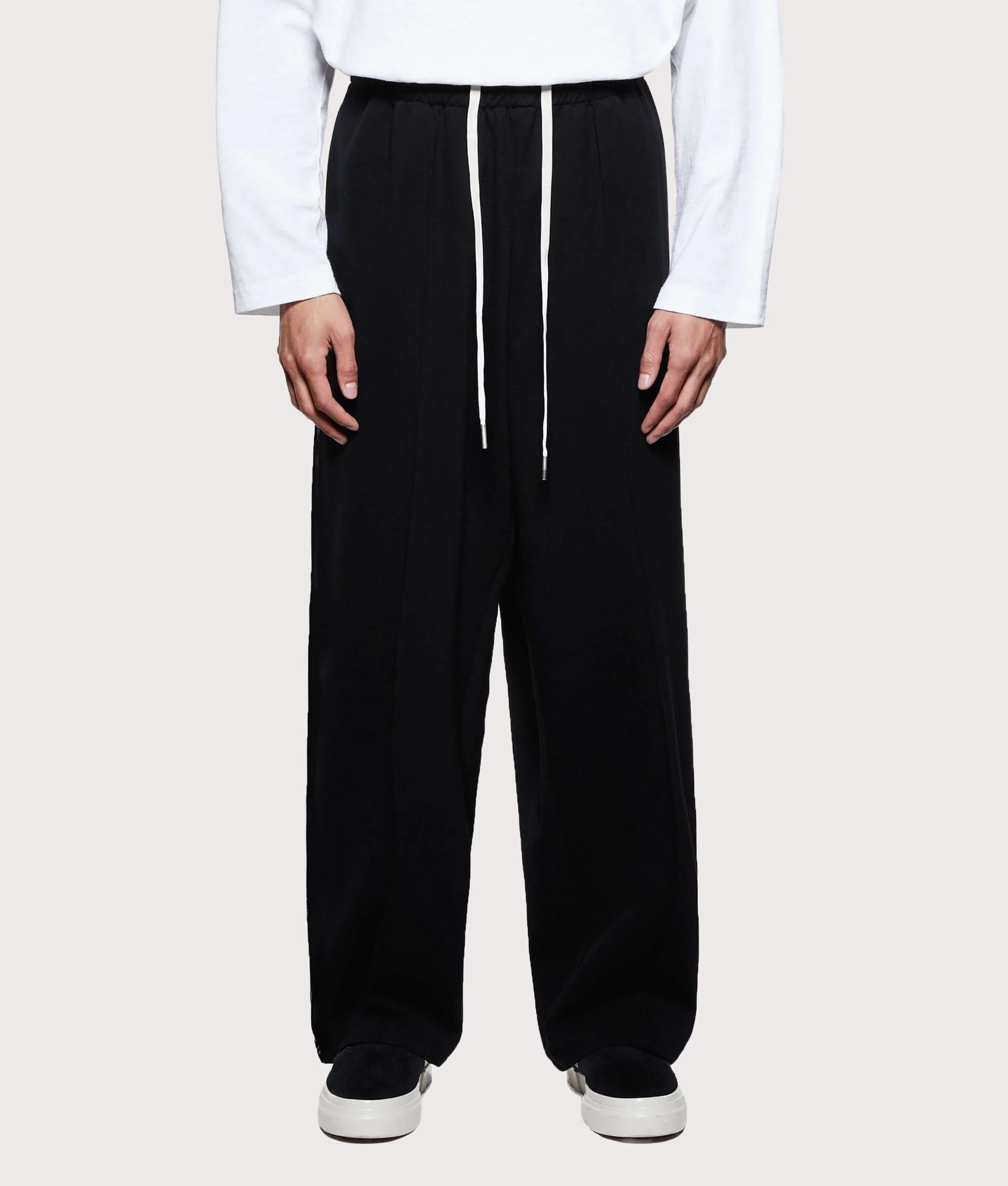 MKI MIYUKI ZOKU Wide Fit Track Pants in core black at EQVVS Menswear. Model front shot.