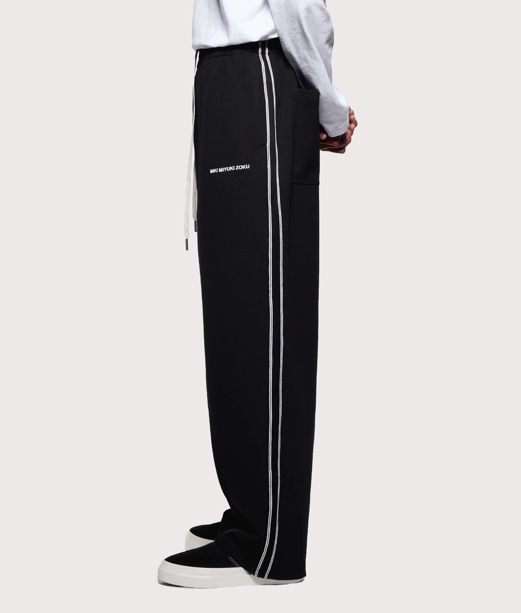 MKI MIYUKI ZOKU Wide Fit Track Pants in core black at EQVVS Menswear. Model side shot.