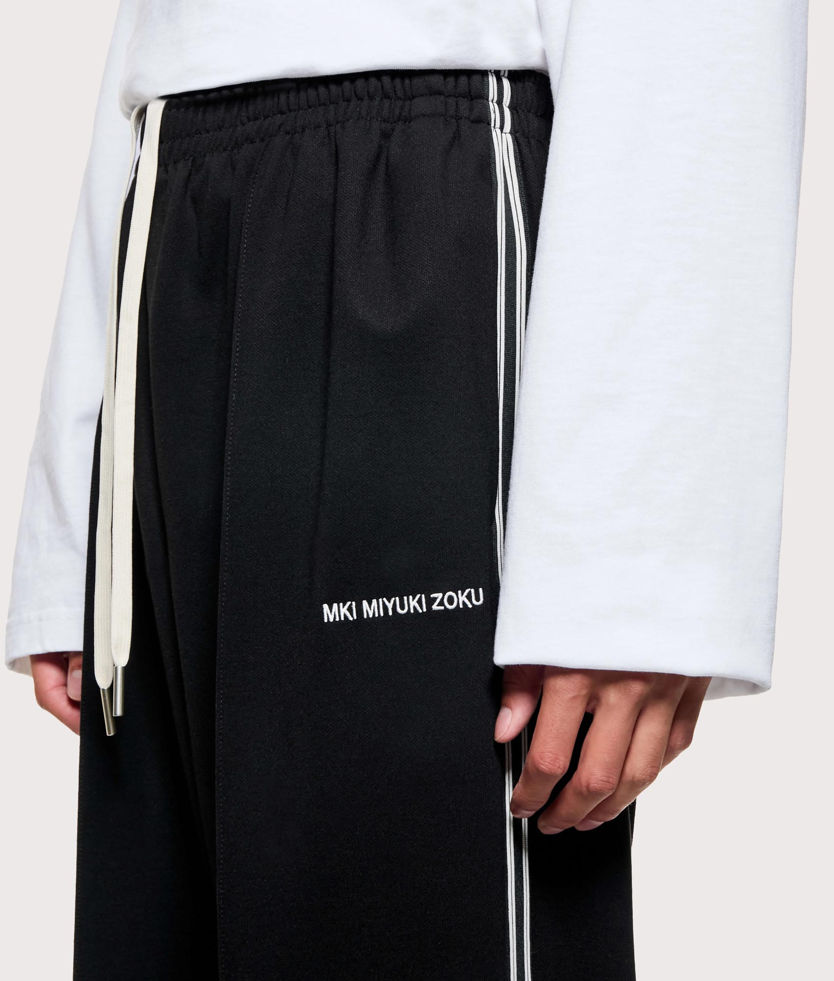 MKI MIYUKI ZOKU Wide Fit Track Pants in core black at EQVVS Menswear. Detail shot.