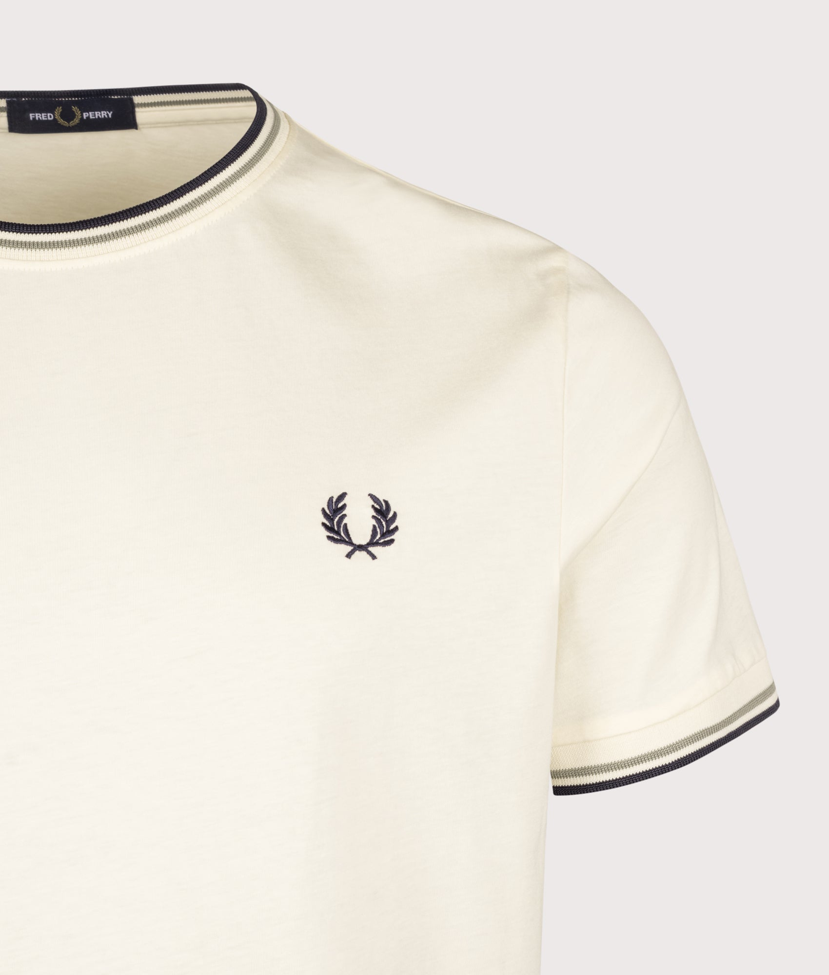Fred Perry look, the Twin Tipped T-Shirt in Ecru, Seagrass and Dark Airforce at EQVVS Menswear. Detail shot. 