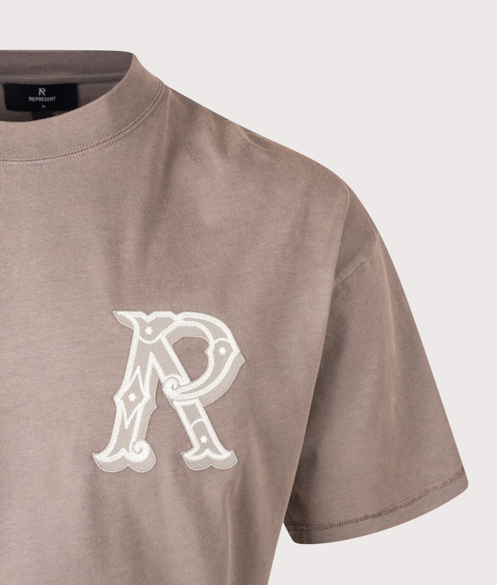 REPRESENT Oversized Fit Western Initial T-Shirt in Dusty Brown at EQVVS Menswear. Detail shot.
