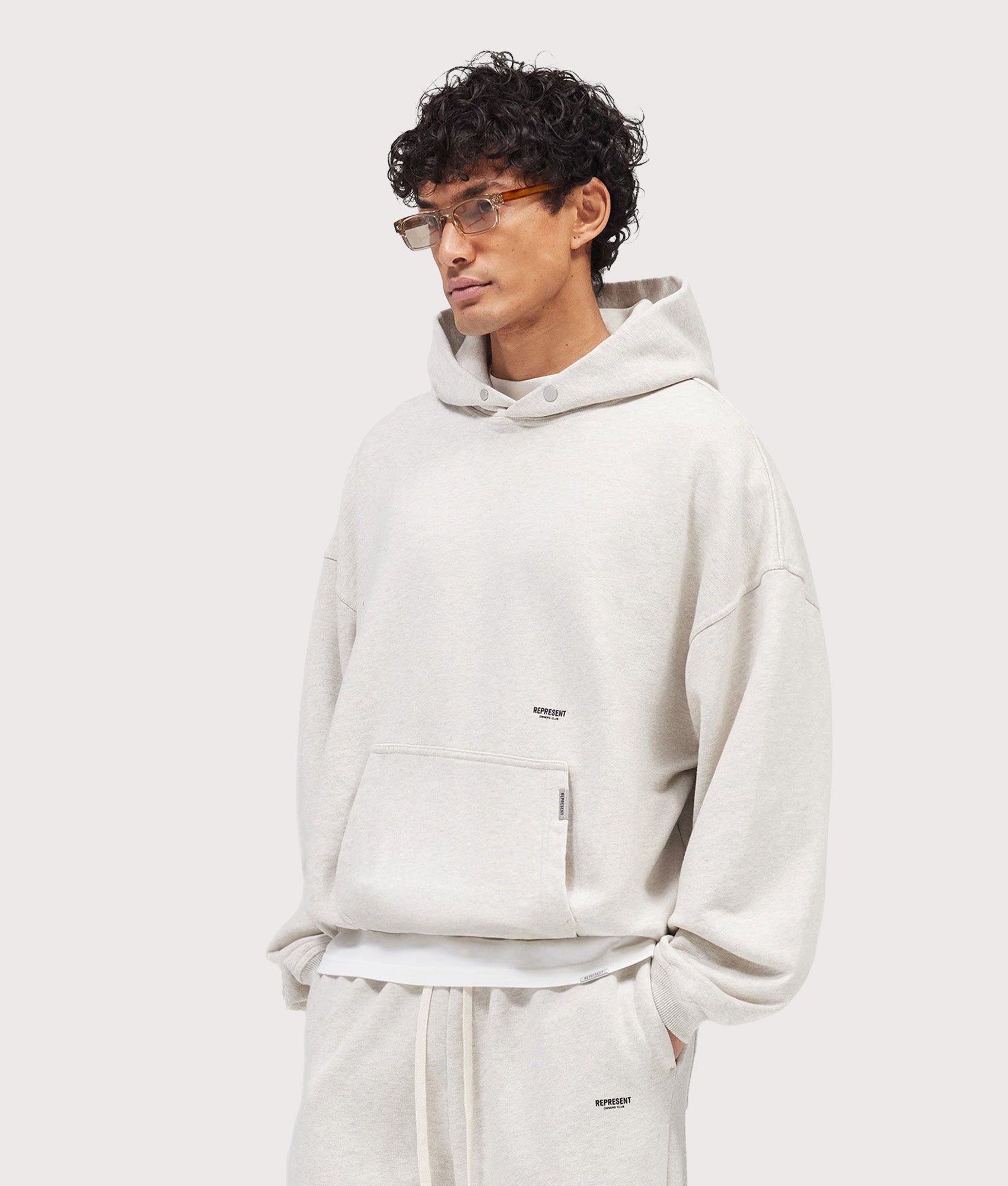 Represent Oversized Micro Owners Club Hoodie in Cream Marl at EQVVS Menswear. Angled model front shot.
