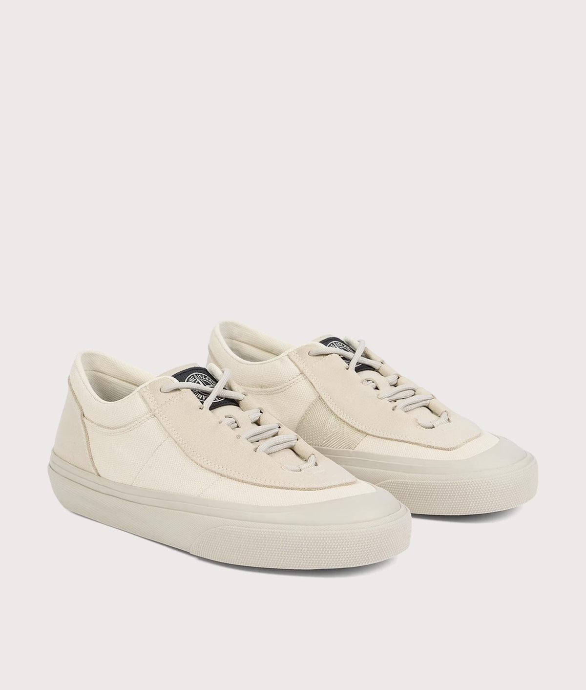 Stone Island Canvas Suede Low Top Trainers in Ivory at EQVVS Menswear. Angled front shot.