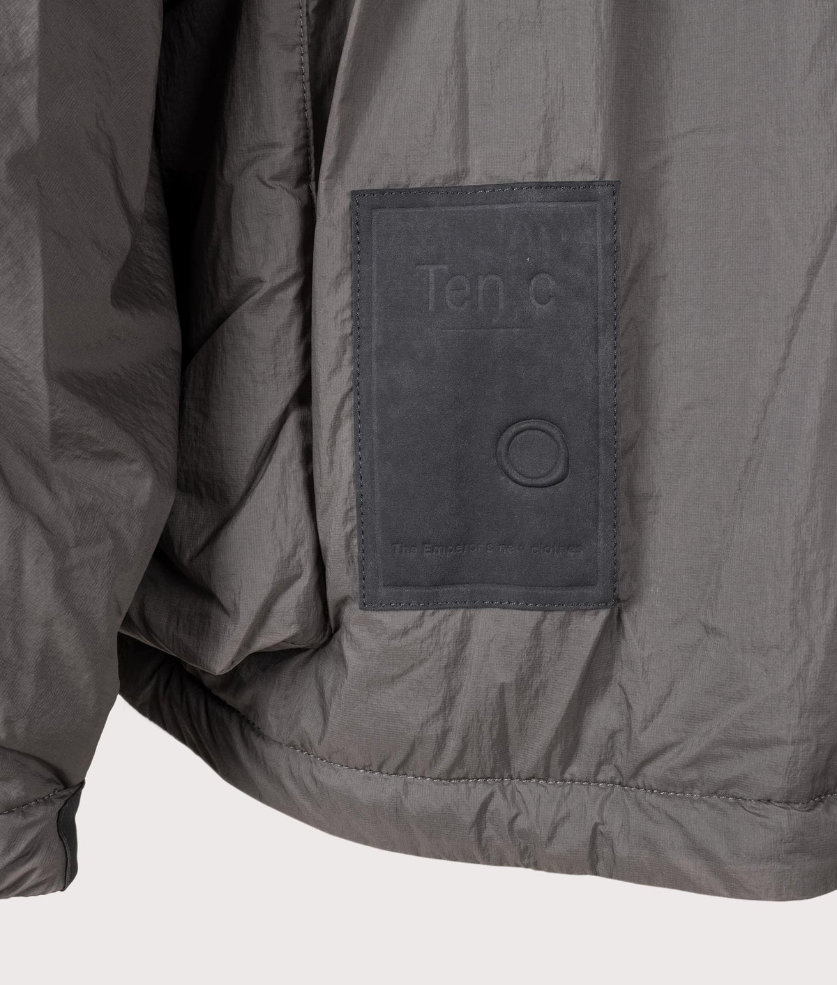 Lightly Padded Skye Ten Anorak Jacket by Ten c in Iron Grey. Shot by EQVVS. Badge detail shot.