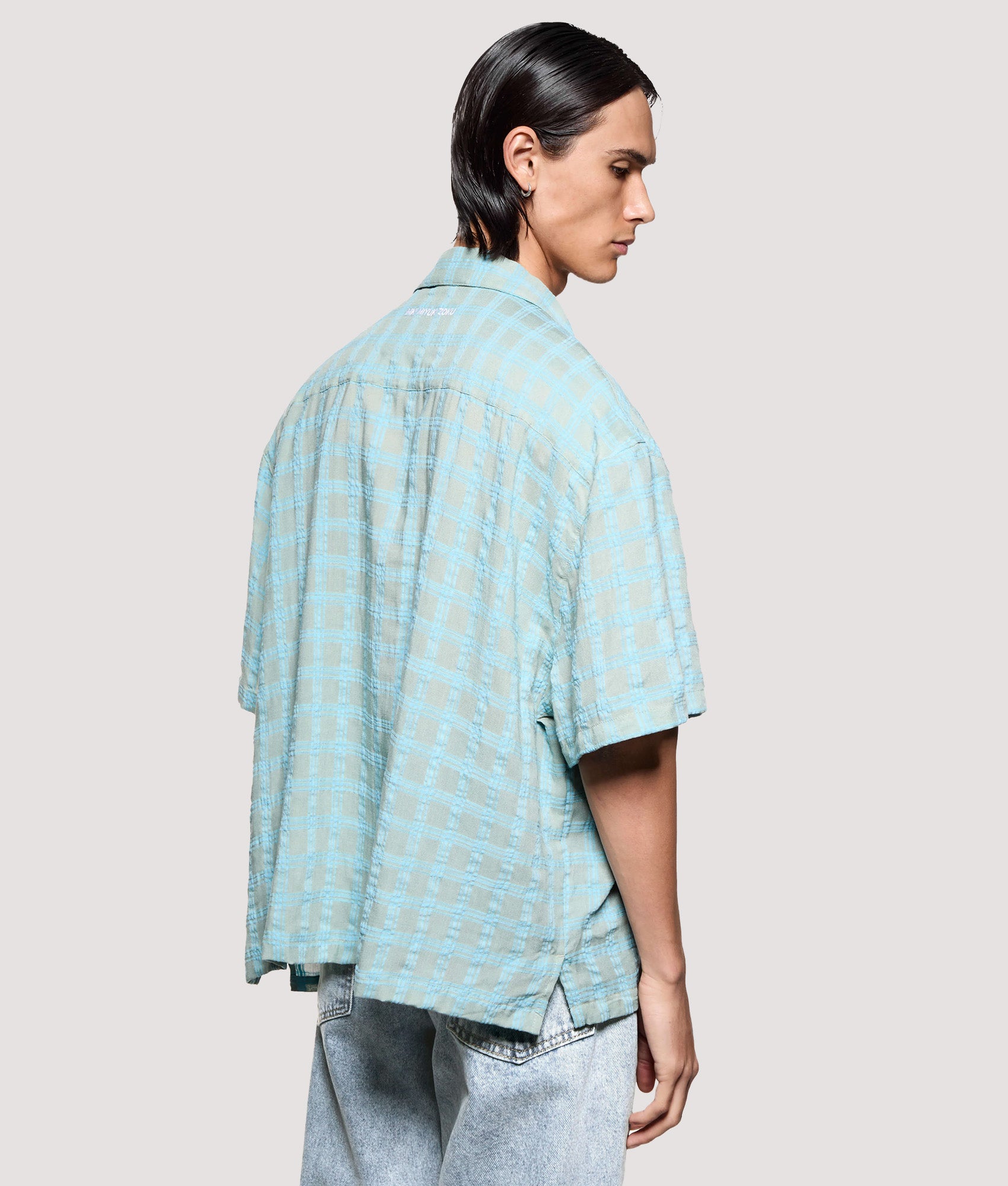 MKI MIYUKI ZOKU Box Fit Grid Check Short Sleeve Vacation Shirt in sage at EQVVS Menswear. Angled model back shot.