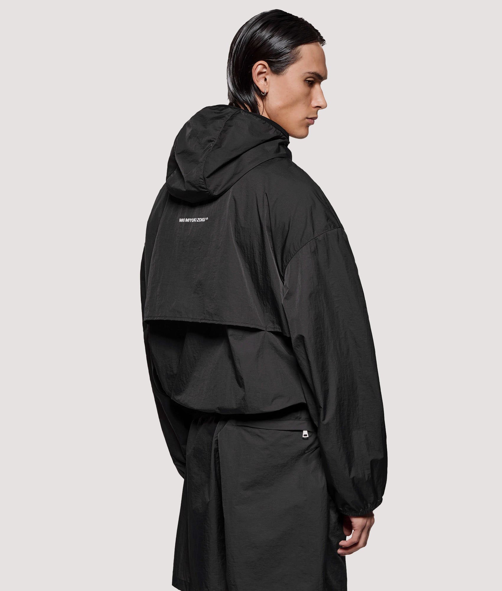 MKI MIYUKI ZOKU Box Fit Hyperlight Hooded Wind Jacket in Black at EQVVS Menswear. Angled model back shot.