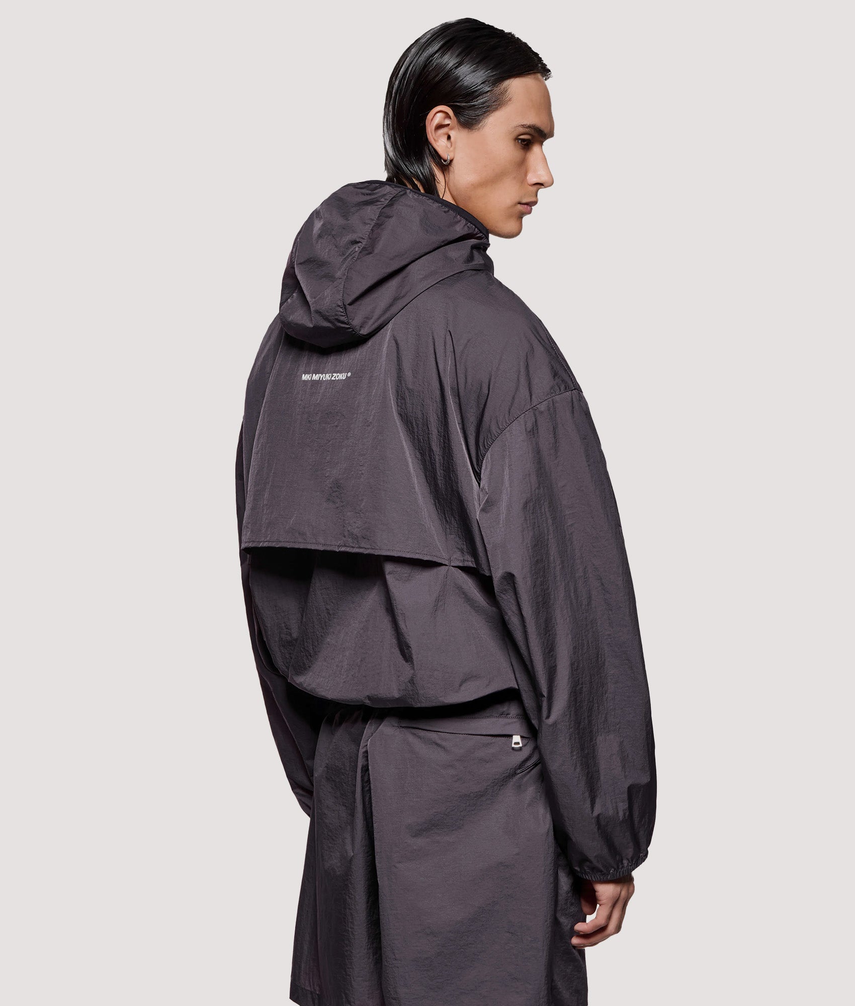 MKI MIYUKI ZOKU Box Fit Hyperlight Hooded Wind Jacket in Raisin at EQVVS Menswear. Angled model back shot.