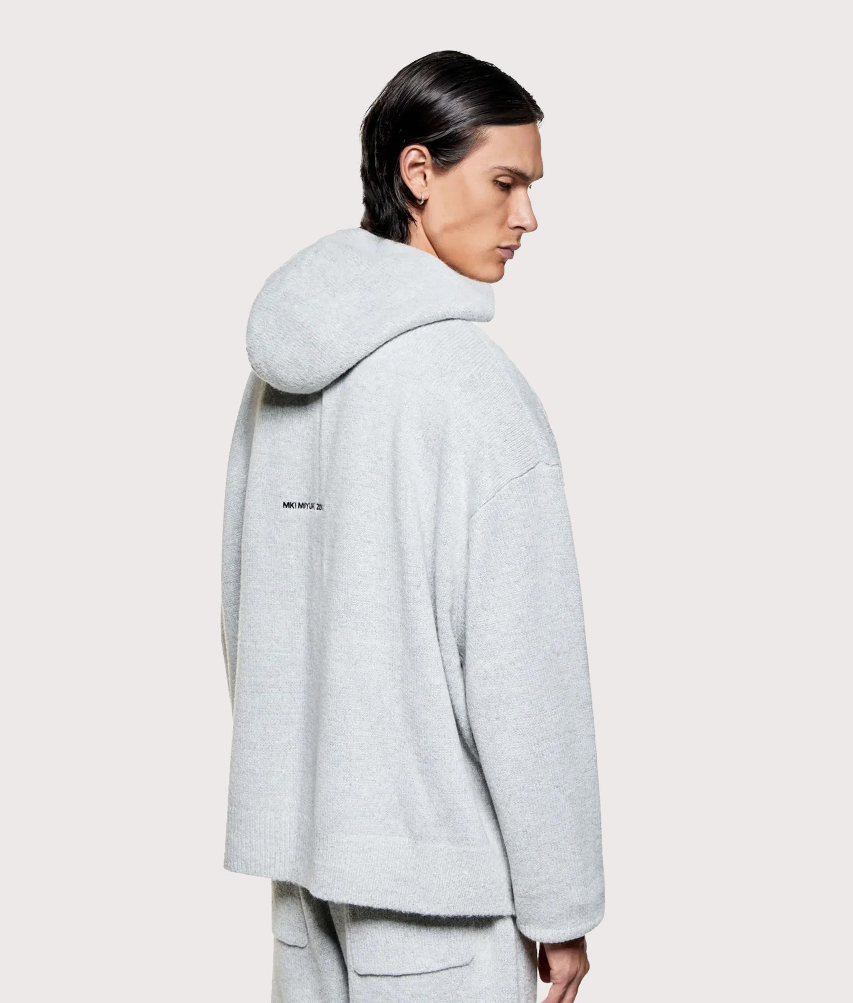 MKI MIYUKI ZOKU Mohair Blend Knit Zip Through Hoodie in Light Grey at EQVVS Menswear. Angled model back shot.
