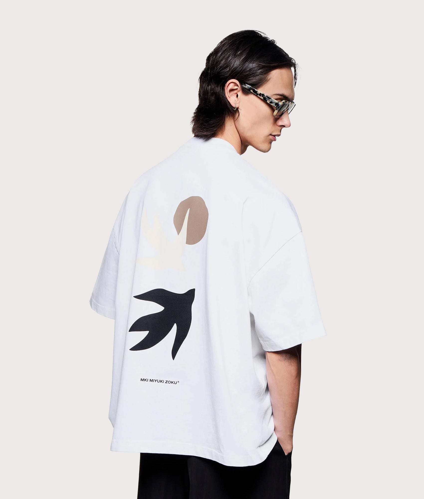 MKI MIYUKI ZOKU Oversized Swallow T-Shirt in White at EQVVS Menswear. Angled model back shot.