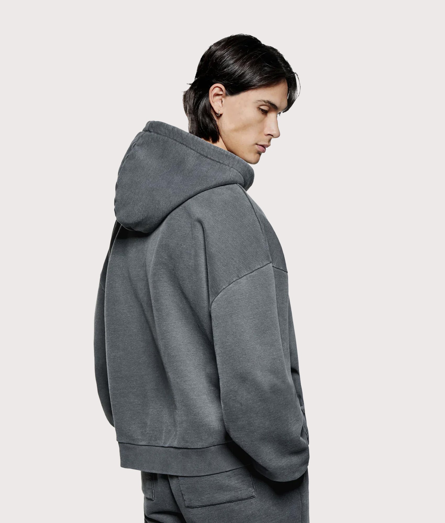 MKI MIYUKI ZOKU Oversized Uniform Zip Through Hoodie in Pigment Black at EQVVS Menswear. Angled model back shot.