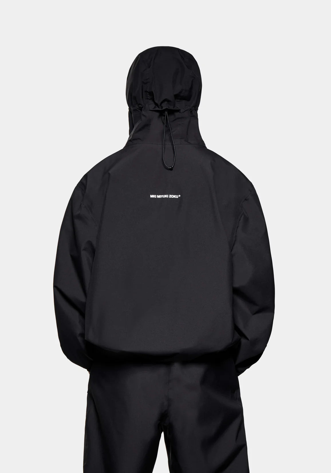 MKI MIYUKI ZOKU Relaxed Fit V2 Shell Hooded Jacket in Black at EQVVS Menswear. Back Model Shot.