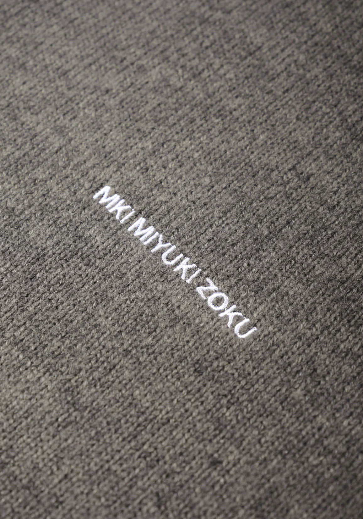 MKI MIYUKI ZOKU Mohair Blend Knit Hoodie in Brown Marl at EQVVS Menswear. Detail Logo Shot. 