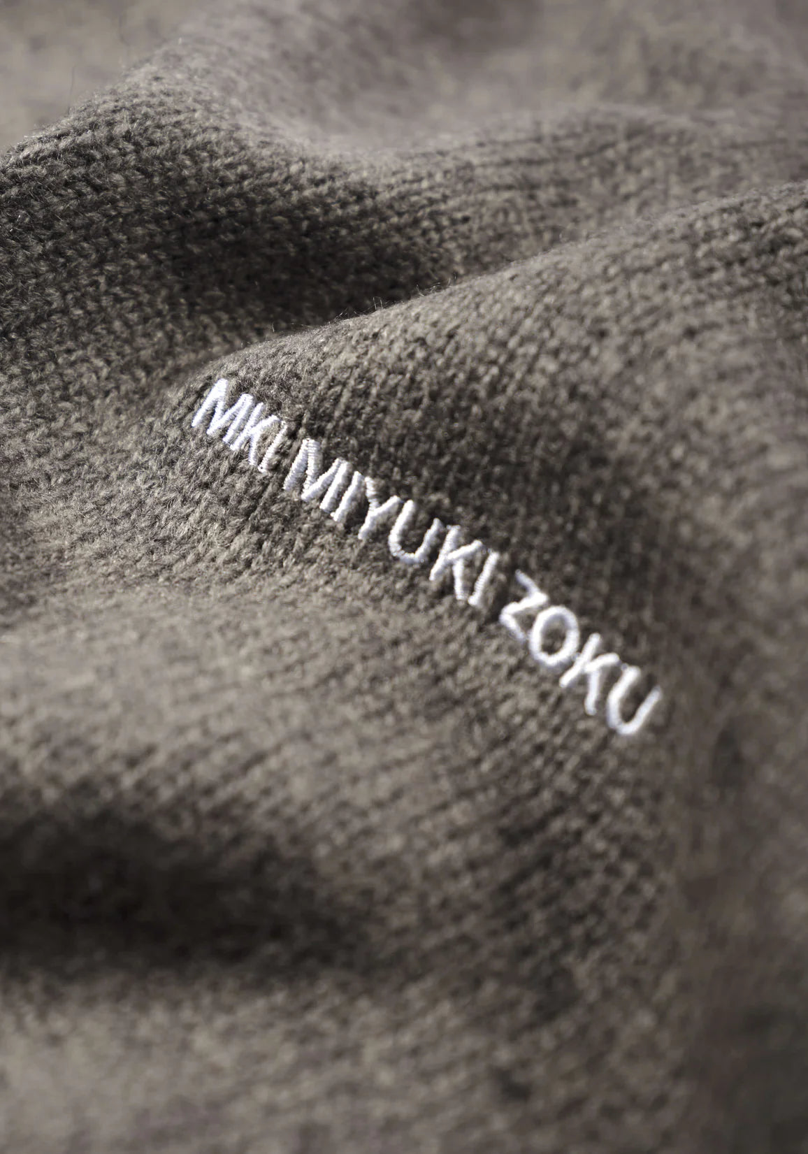 MKI MIYUKI ZOKU Mohair Blend Knit Hoodie in Brown Marl at EQVVS Menswear. Detail Logo Shot. 