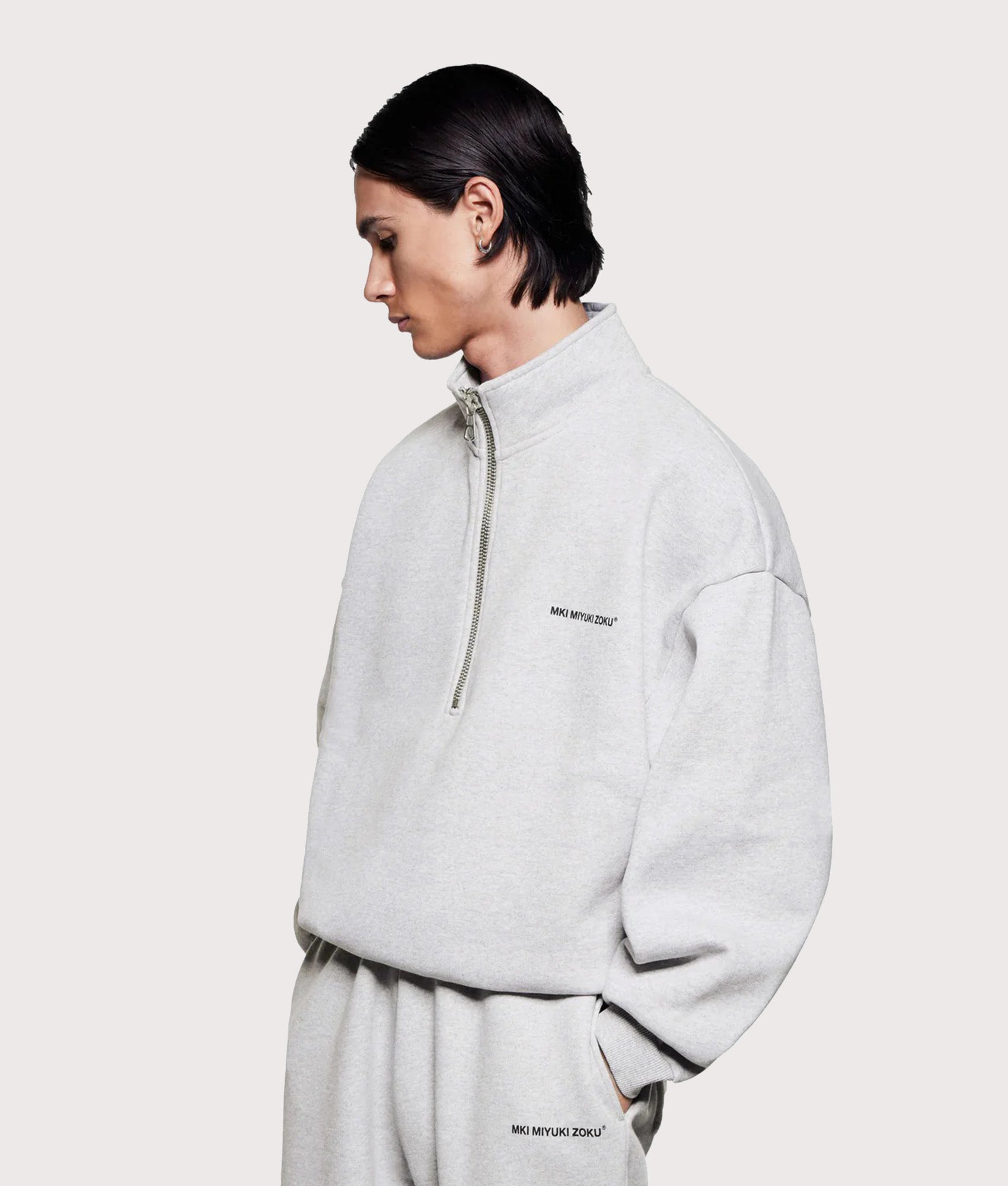 MKI MIYUKI ZOKU Oversized Uniform Quarter Zip Sweatshirt in Grey at EQVVS Menswear. Angled model front shot.