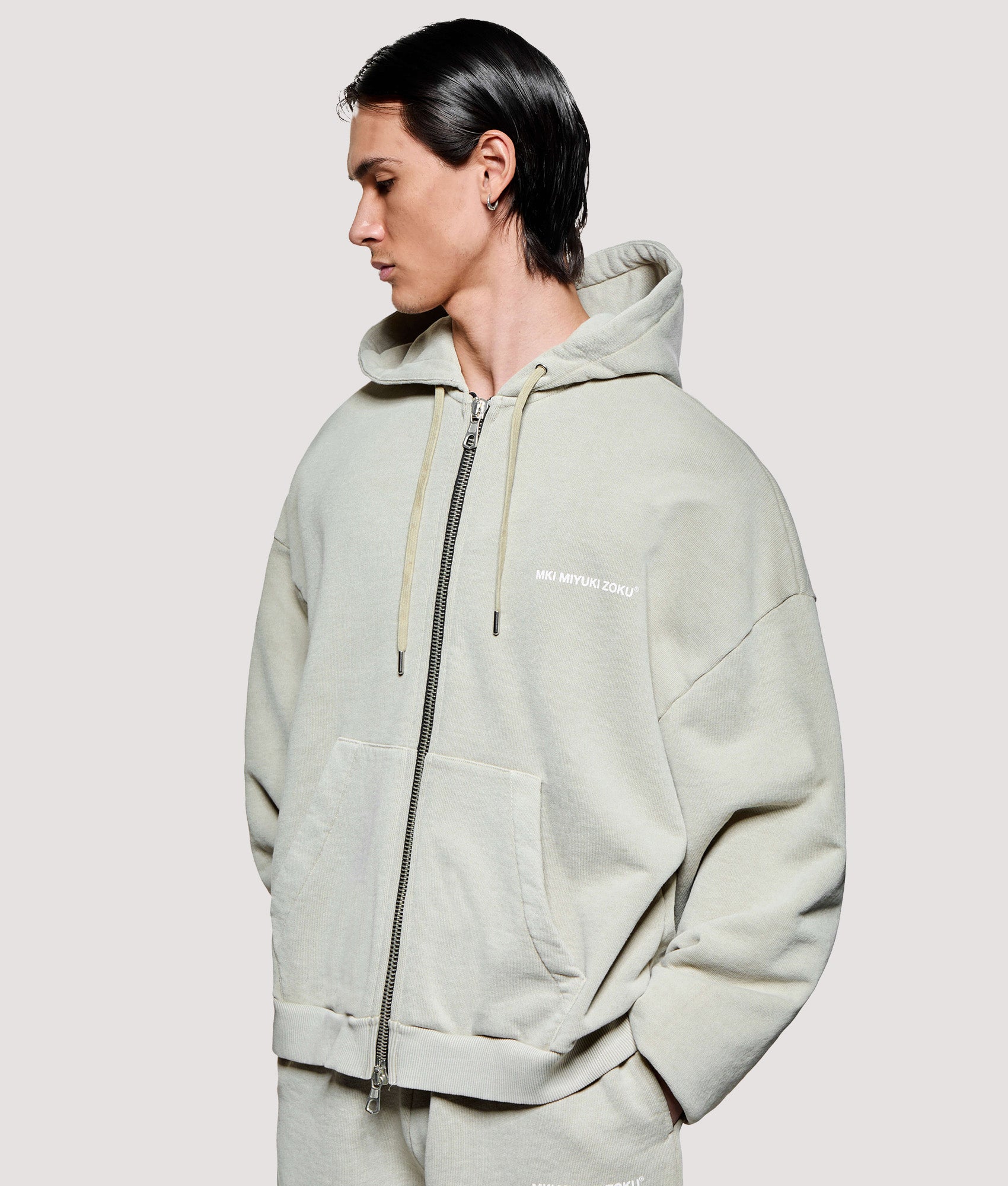 MKI MIYUKI ZOKU Box Fit Uniform Zip Through Hoodie in Pigment Cement at EQVVS Menswear. Angled model front shot.