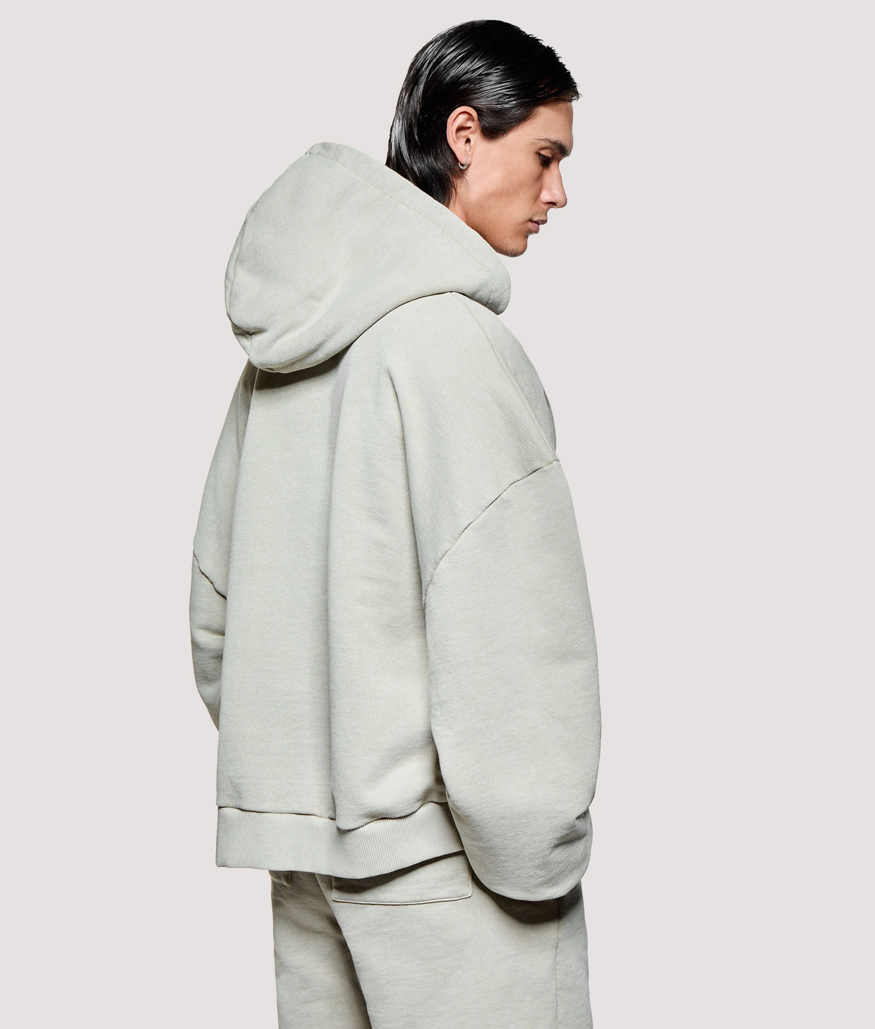 MKI MIYUKI ZOKU Box Fit Uniform Zip Through Hoodie in Pigment Cement at EQVVS Menswear. Angled model back shot.